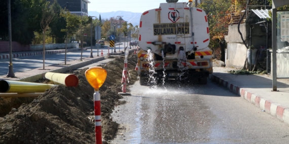 Muhtar, toz çıkmasın diye caddeyi suluyor